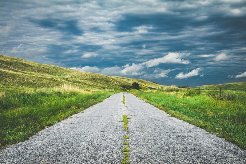 A quiet country road stretching into the distance through green hills, symbolizing life direction and choices